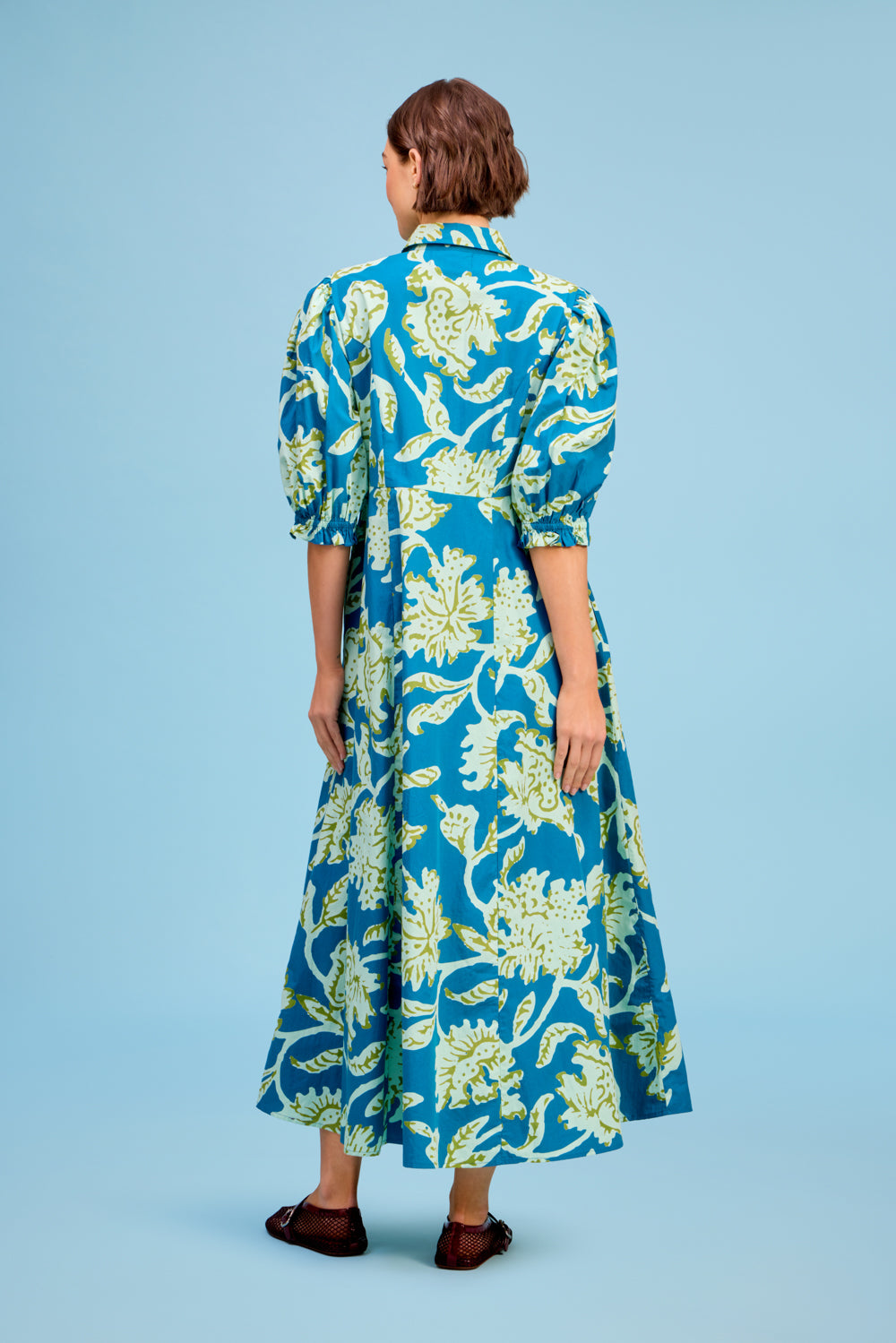 Back view of LIVRO Rosie Dress featuring a vibrant blue and yellow botanical print, puff sleeves and long flowing skirt.