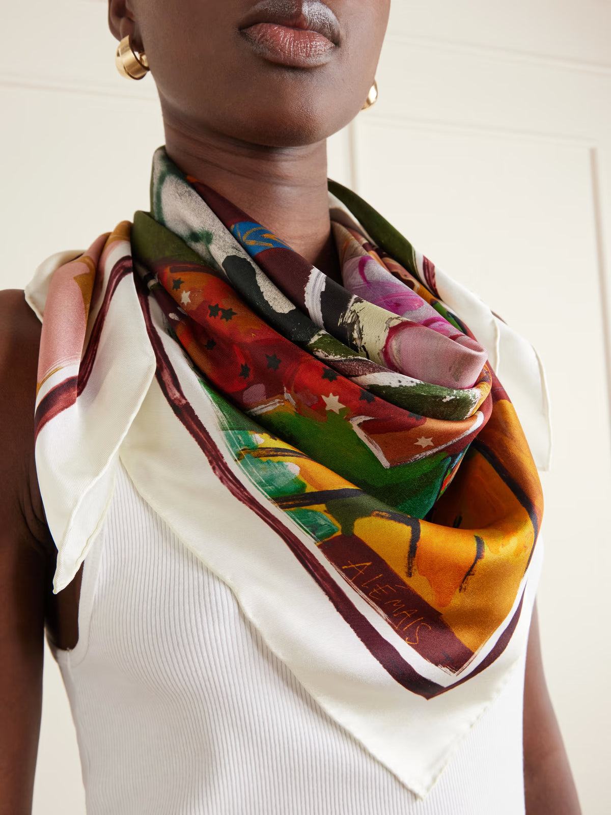 ALEMAIS Mlak Silk Scarf tied around neck featuring vibrant green, orange, and pink print.
